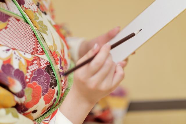 短冊に筆で書く着物姿の人。短冊と筆。
